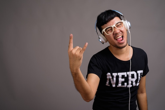 Jonge Aziatische nerd man luisteren naar muziek tegen grijs