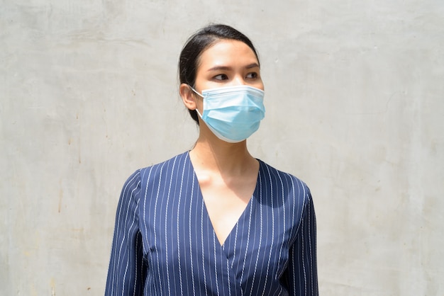 Jonge Aziatische onderneemster met masker voor bescherming tegen de uitbraak die van het coronavirus in openlucht denken