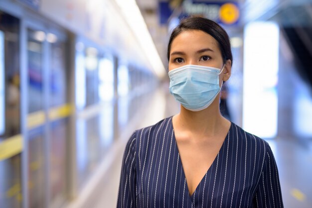 Jonge Aziatische onderneemster met masker voor bescherming tegen de uitbraak van het coronavirus die bij het metrostation wachten