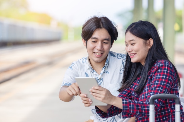 Jonge Aziatische paar-backpacker die tablet gebruikt voor het vinden van een bestemmingsreis op het treinstation railway