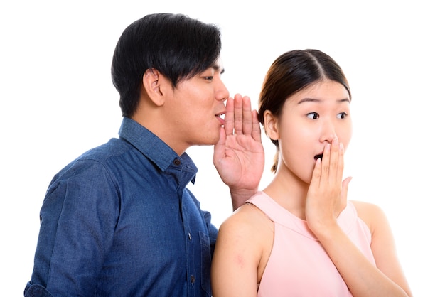 jonge Aziatische paar met man fluisteren vrouw op zoek geschokt