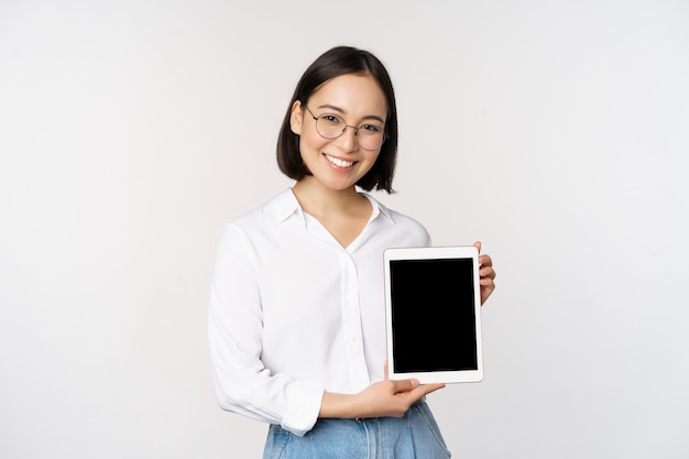 Jonge aziatische professionele vrouw demonstreert informatie op het digitale tabletscherm over haar gadget die lacht en kijkt naar de camera die op een witte achtergrond staat