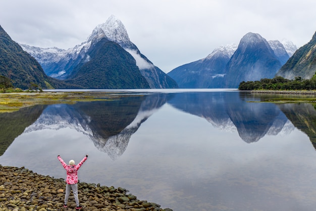 Foto jonge aziatische reiziger viert succes bij milford sound, fiordland national park, south island, nieuw-zeeland