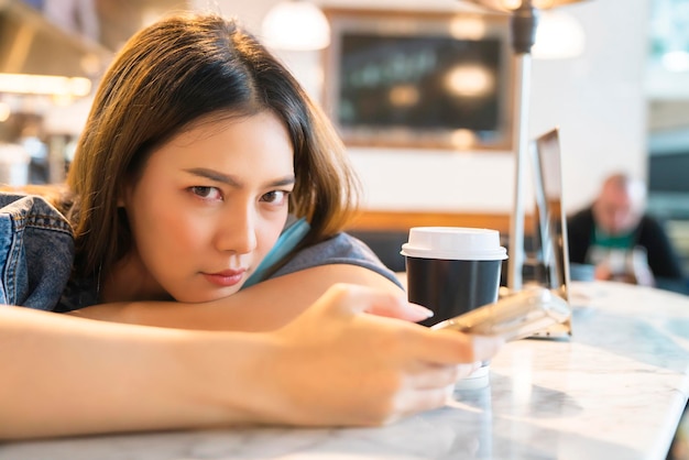 Jonge aziatische reizigersvrouw zit ontspannen gezichtsuitdrukking handgebruik smartphone wachtend op tijd aan boord in café-restaurant op de vertrekterminal van de luchthaven