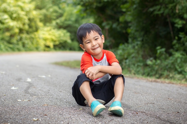 Jonge Aziatische schattige jongen zittend op weg in park.