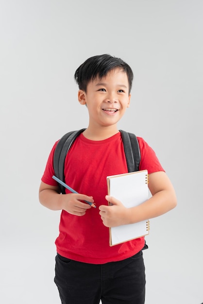 Jonge Aziatische schooljongen schrijven in Kladblok met rugzak op witte achtergrond writing