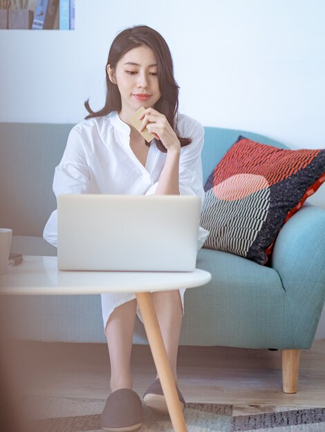 Jonge Aziatische schoonheid online winkelen met creditcard en laptop thuis