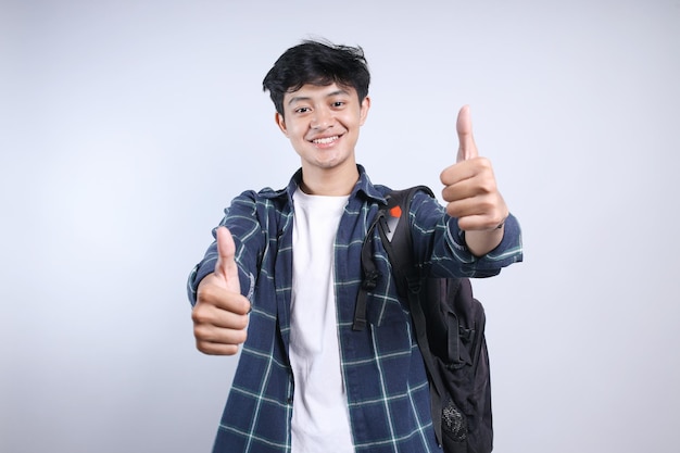 Jonge Aziatische student draagt een rugzak en toont twee duimen naar de camera.