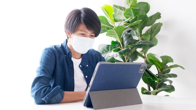 Jonge aziatische studentenmens die een beschermingsmasker draagt dat met een laptop werkt terwijl hij online studeert