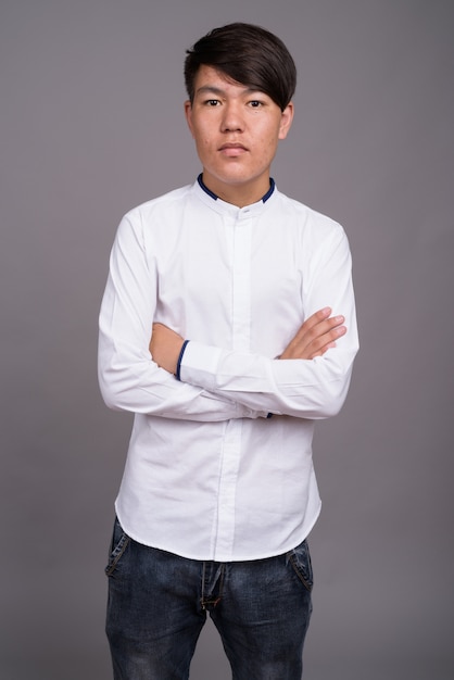 jonge Aziatische tiener die slimme vrijetijdskleding draagt tegen grijze muur