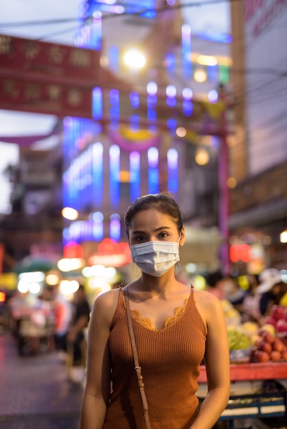 Jonge aziatische toeristenvrouw die masker draagt ter bescherming tegen de uitbraak van het coronavirus in chinatown 's nachts