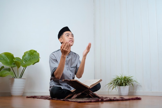 Jonge aziatische trouwe moslim man bidt thuis op het gebedskleed met de koran op ramadan kareem