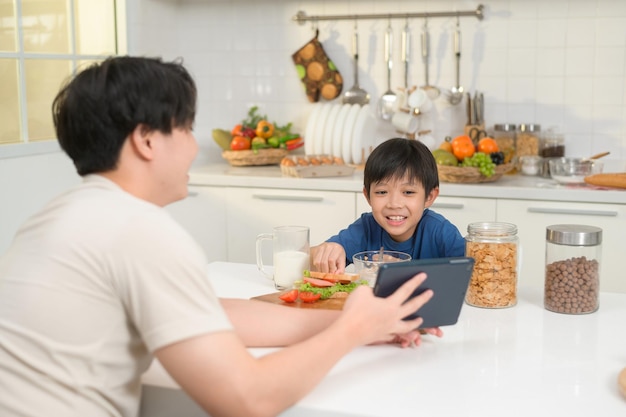 Jonge Aziatische vader en zijn zoon die digitale tablet gebruiken die samen genieten in de keuken thuis