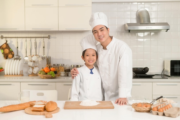 Jonge Aziatische vader en zijn zoon dragen chef-kok uniform bakken samen in de keuken thuis