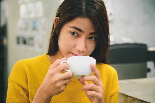 jonge Aziatische volwassen vrouw drinken koffie glimlachend in café.