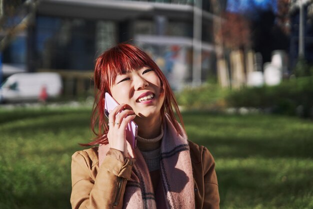 Jonge aziatische vrouw belt terwijl ze op een mobiele smartphone praat en op straat loopt