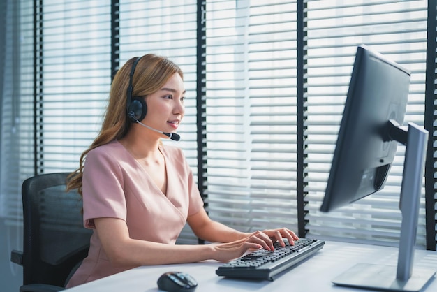 Jonge Aziatische vrouw callcenter operator in headset in gesprek met klant op kantoor