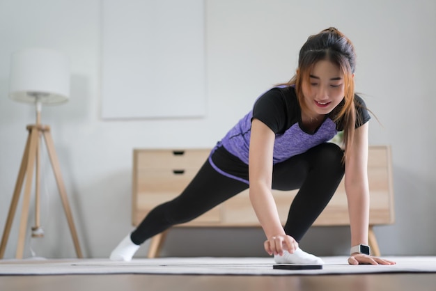 Jonge Aziatische vrouw controleert workouttijd op haar smartphone terwijl ze oefent met een gezonde levensstijl