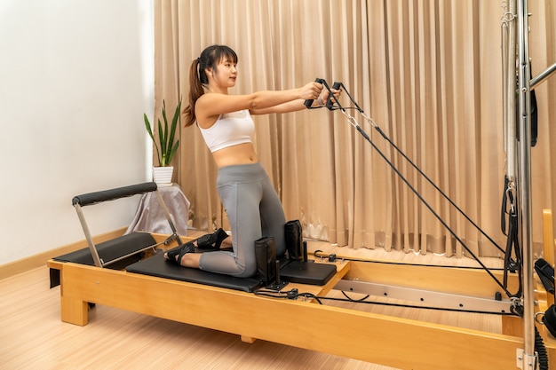 Foto jonge aziatische vrouw die aan de pilates-reformer-machine werkt tijdens haar training voor gezondheidsoefeningen