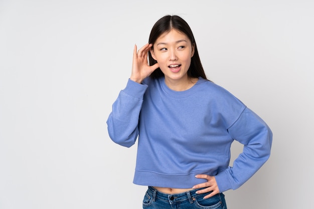 Jonge Aziatische vrouw die bij het luisteren aan iets wordt geïsoleerd door hand op het oor te zetten