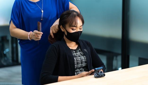 Jonge Aziatische vrouw die bij kapsalon chirurgisch beschermend gezichtsmasker draagt. Nieuw normaal en sociaal afstandsconcept