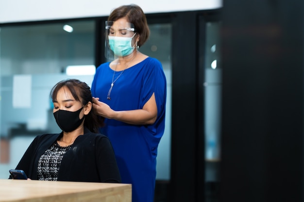 Jonge Aziatische vrouw die bij kapsalon chirurgisch beschermend gezichtsmasker draagt. Nieuw normaal en sociaal afstandsconcept