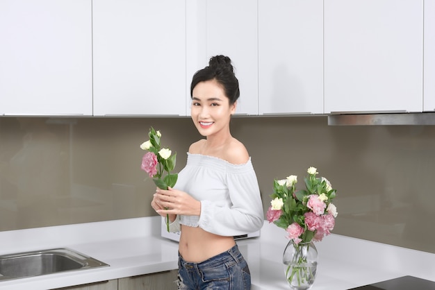 Jonge Aziatische vrouw die bloemen in de keuken schikt.