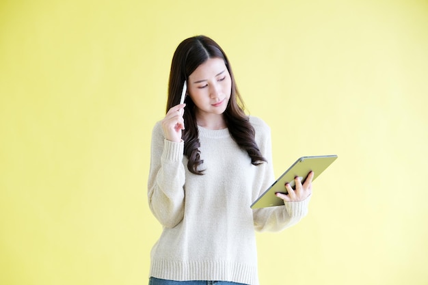 Jonge aziatische vrouw die digitale tablet gebruikt terwijl ze over een geïsoleerde gele achtergrond staat