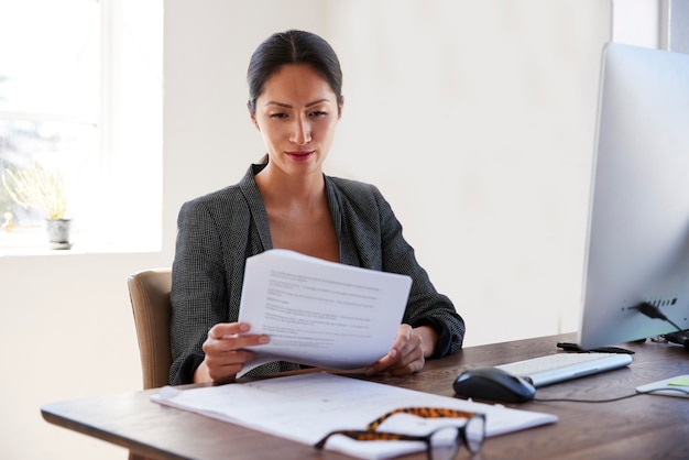 Jonge Aziatische vrouw die documenten leest aan haar bureau in een kantoor