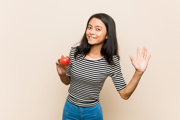 Jonge Aziatische vrouw die een appel houdt die een prettige verrassing ontvangt, opgewekt en handen opheft.