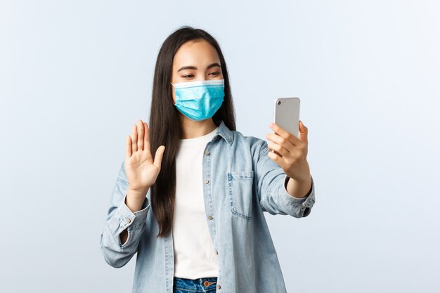 Jonge Aziatische vrouw die een beschermend masker draagt dat een telefoon houdt