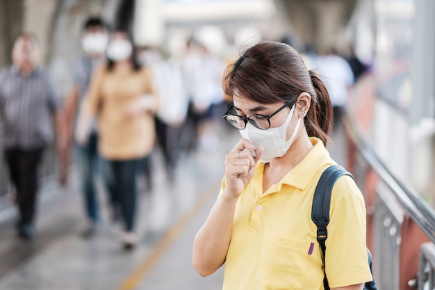 Jonge Aziatische vrouw die een beschermingsmasker draagt tegen het nieuwe coronavirus (2019-nCoV) of het Wuhan-coronavirus op het openbare treinstation, is een besmettelijk virus dat infecties van de luchtwegen veroorzaakt.