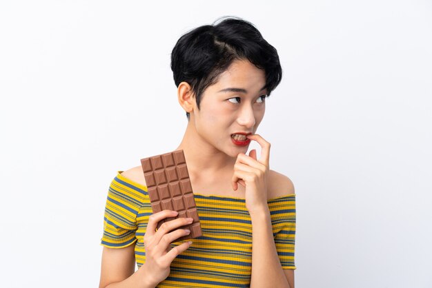 Jonge Aziatische vrouw die een chocoladetablet neemt en twijfels heeft