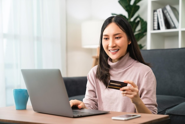 Jonge Aziatische vrouw die een creditcard vasthoudt en een laptop gebruikt om online te winkelen met betaling via internetbankieren