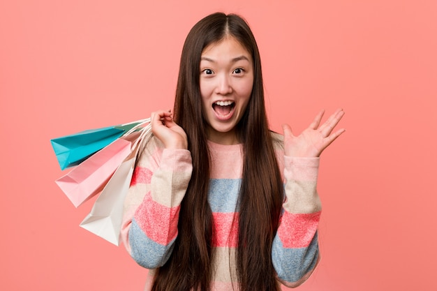 Jonge Aziatische vrouw die een het winkelen zak houdt die een overwinning of een succes viert