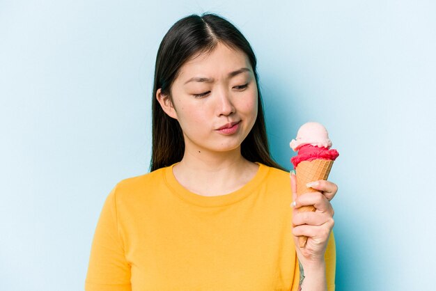 Jonge Aziatische vrouw die een ijsje eet dat op blauwe achtergrond wordt geïsoleerd