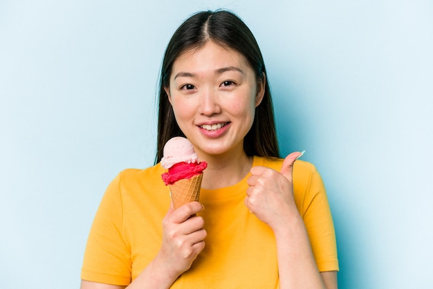 Jonge Aziatische vrouw die een ijsje eet dat op blauwe achtergrond wordt geïsoleerd