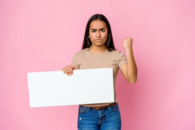 Jonge Aziatische vrouw die een leeg document voor wit houdt iets over geïsoleerde muur die vuist, agressieve gezichtsuitdrukking toont.