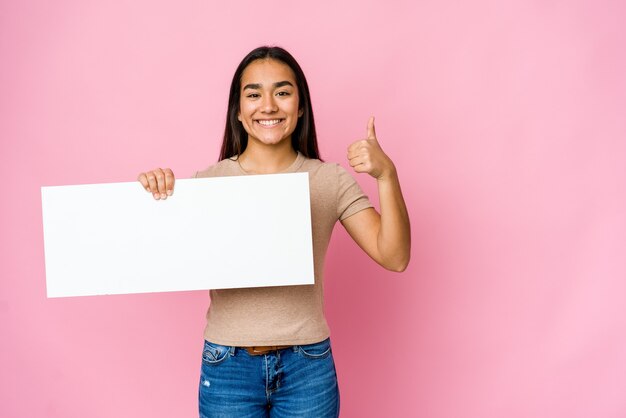 Jonge Aziatische vrouw die een leeg document voor wit iets over geïsoleerde muur houdt die en duim opheft