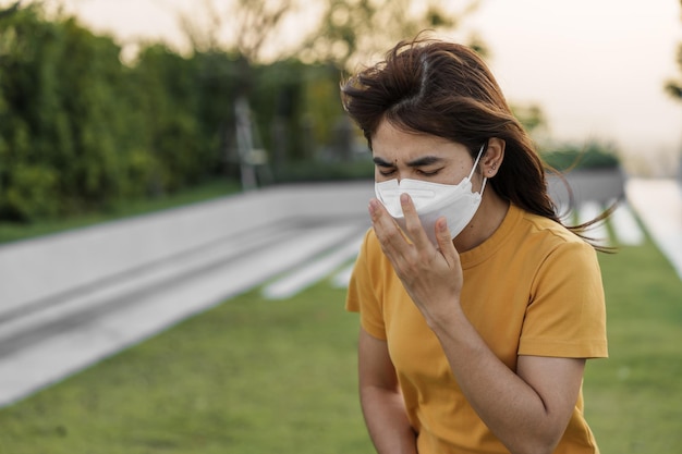 Jonge aziatische vrouw die een n95-ademhalingsmasker draagt, beschermt en filtert pm25 of fijnstof tegen slechte luchtverontreiniging in de luchtkwaliteitsindex van de stad aqi ongezond zorgconcept