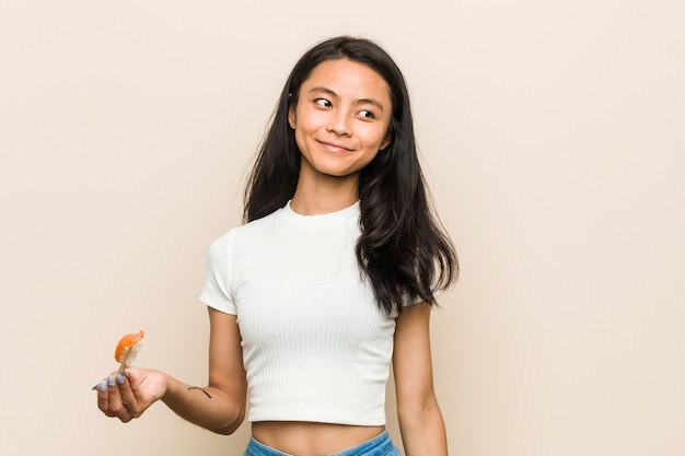 Jonge Aziatische vrouw die een sushistuk houdt dat zeker met gekruiste wapens glimlacht.