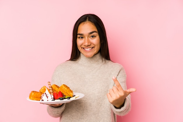 Jonge Aziatische vrouw die een wafel houdt wijzend met vinger naar u alsof uitnodigend dichterbij komt.