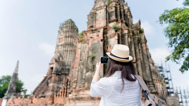 Foto jonge aziatische vrouw die foto maakt op zijn mobiele telefooncamera van een prachtig landschap terwijl hij in de buurt van de tempel staat