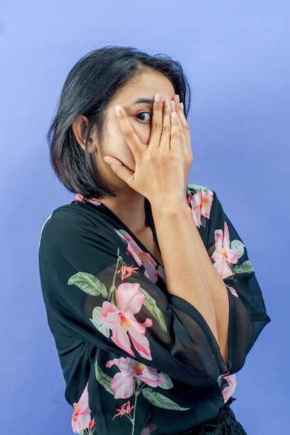 Jonge Aziatische vrouw die gezicht bedekt met handen die tussen vingers gluren met angstexpressie