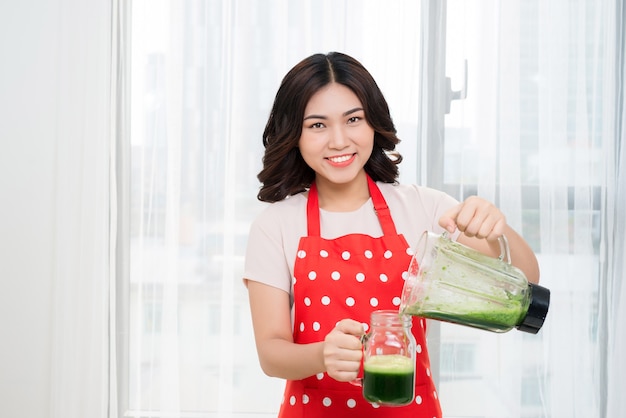 Jonge aziatische vrouw die groene detox-smoothie in de keuken thuis maakt.