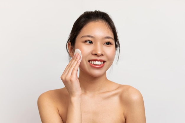 Jonge aziatische vrouw die haar gezicht schoonmaakt met wattenschijfjes