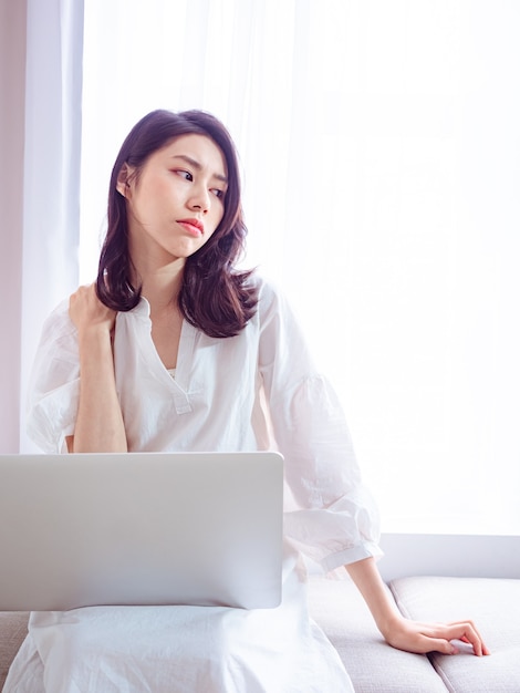 Jonge aziatische vrouw die lijdt aan pijn in de schouder bij het gebruik van een laptop