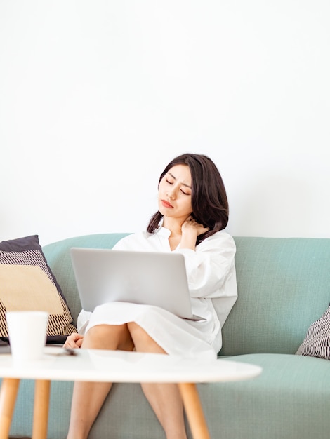 Jonge aziatische vrouw die lijdt aan pijn in de schouder bij het gebruik van een laptop