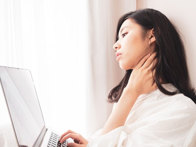 Jonge aziatische vrouw die lijdt aan pijn in de schouder bij het gebruik van een laptop