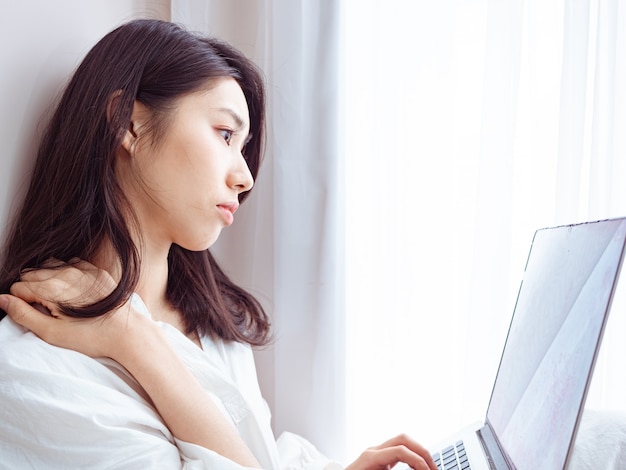 Jonge aziatische vrouw die lijdt aan pijn in de schouder bij het gebruik van een laptop